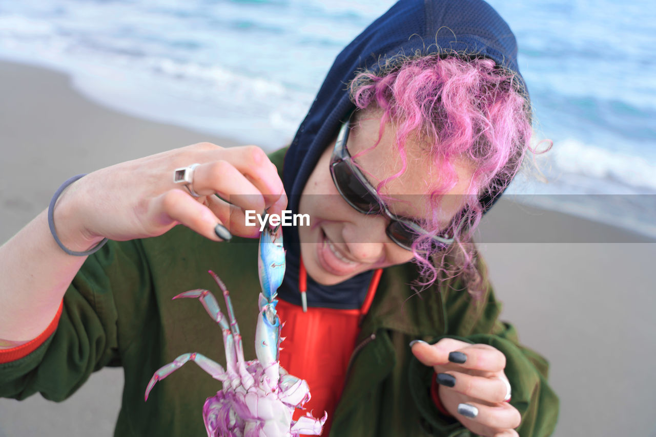 Smiling woman with dyed hair holding dead crab at beach