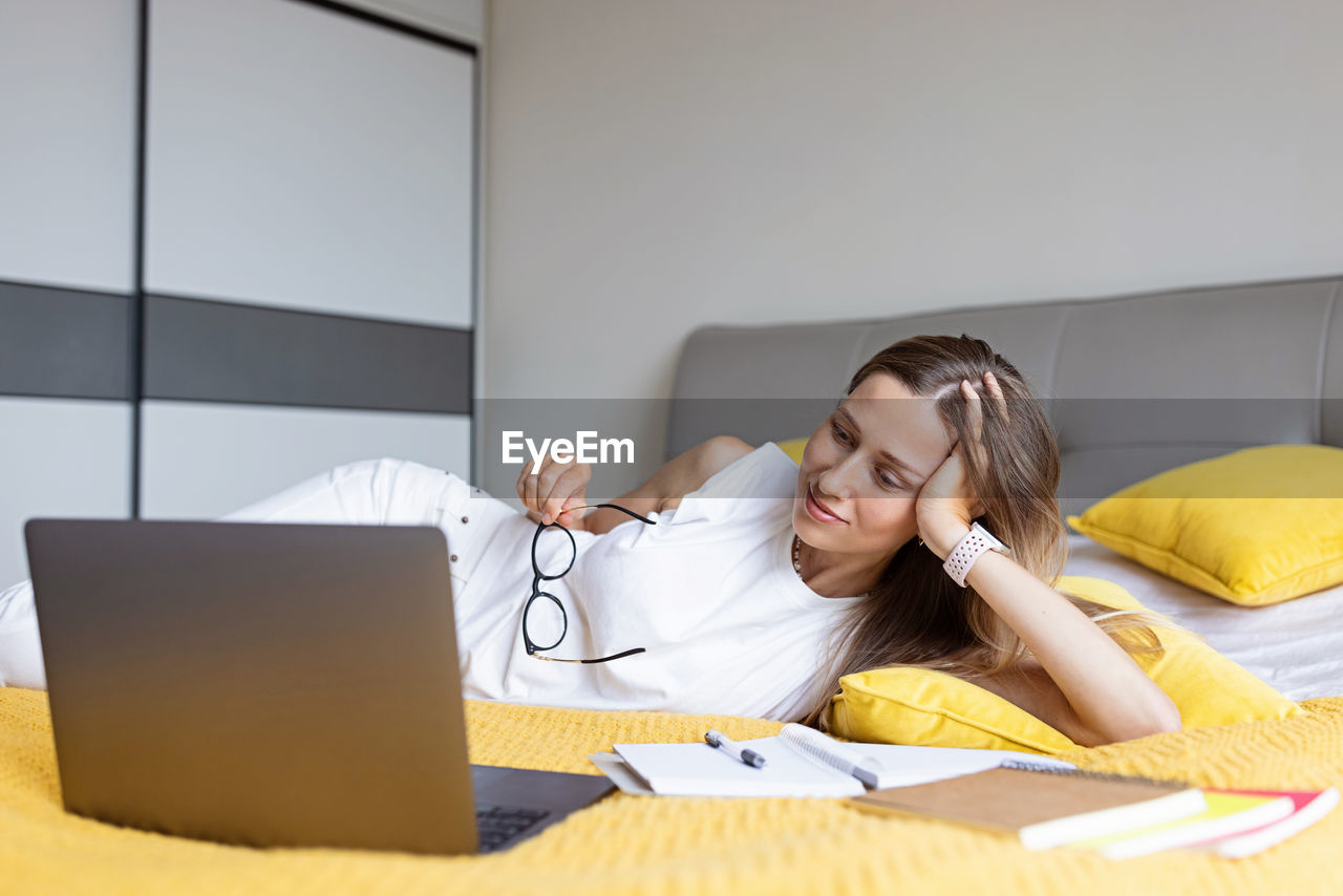 Smiling woman talking on video call while lying on bed at home