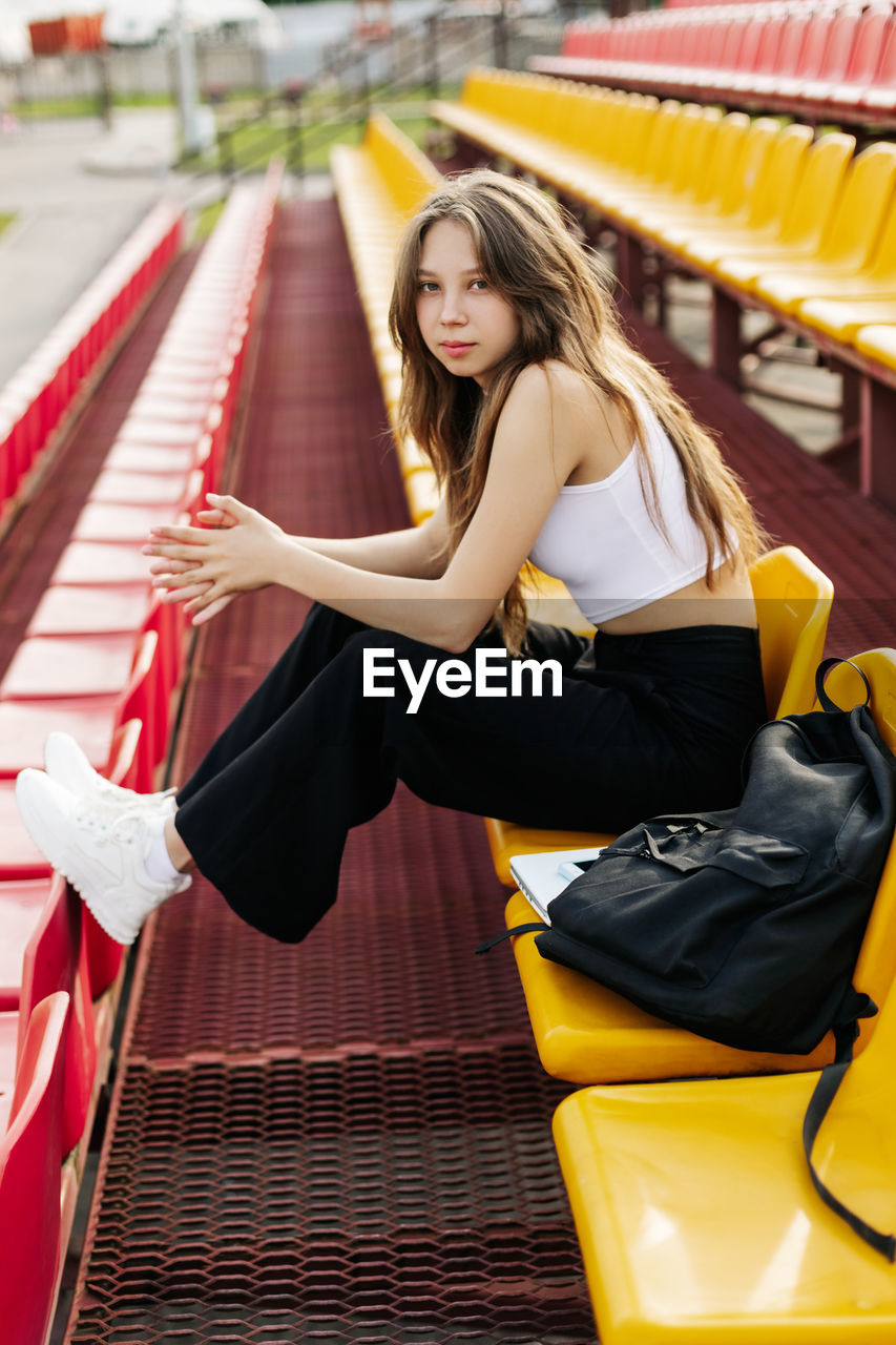 A smiling teenage girl is sitting on the podium next to her school backpack