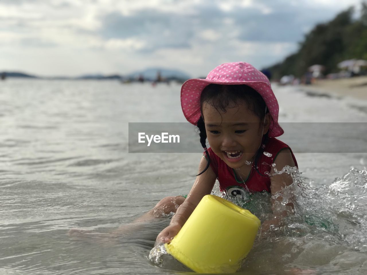 Girl playing with bucket while sitting at beach