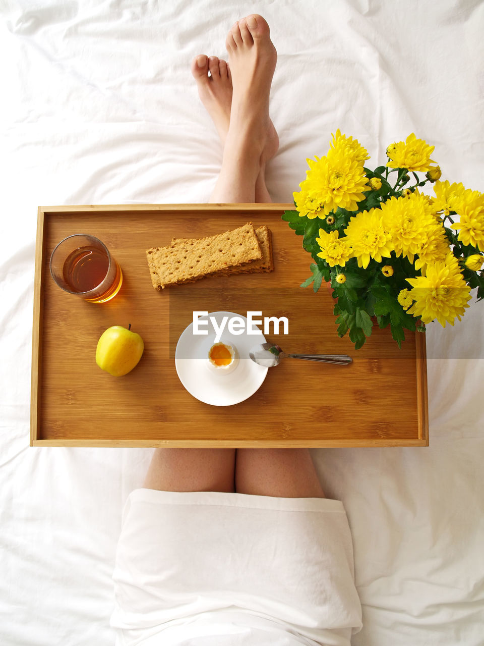 Low section of woman with egg and drink on bed at home