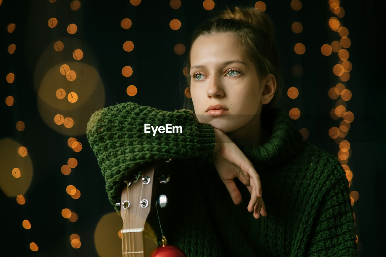 A beautiful teenager girl dreamily looks to the side, leaning on the neck of a guitar