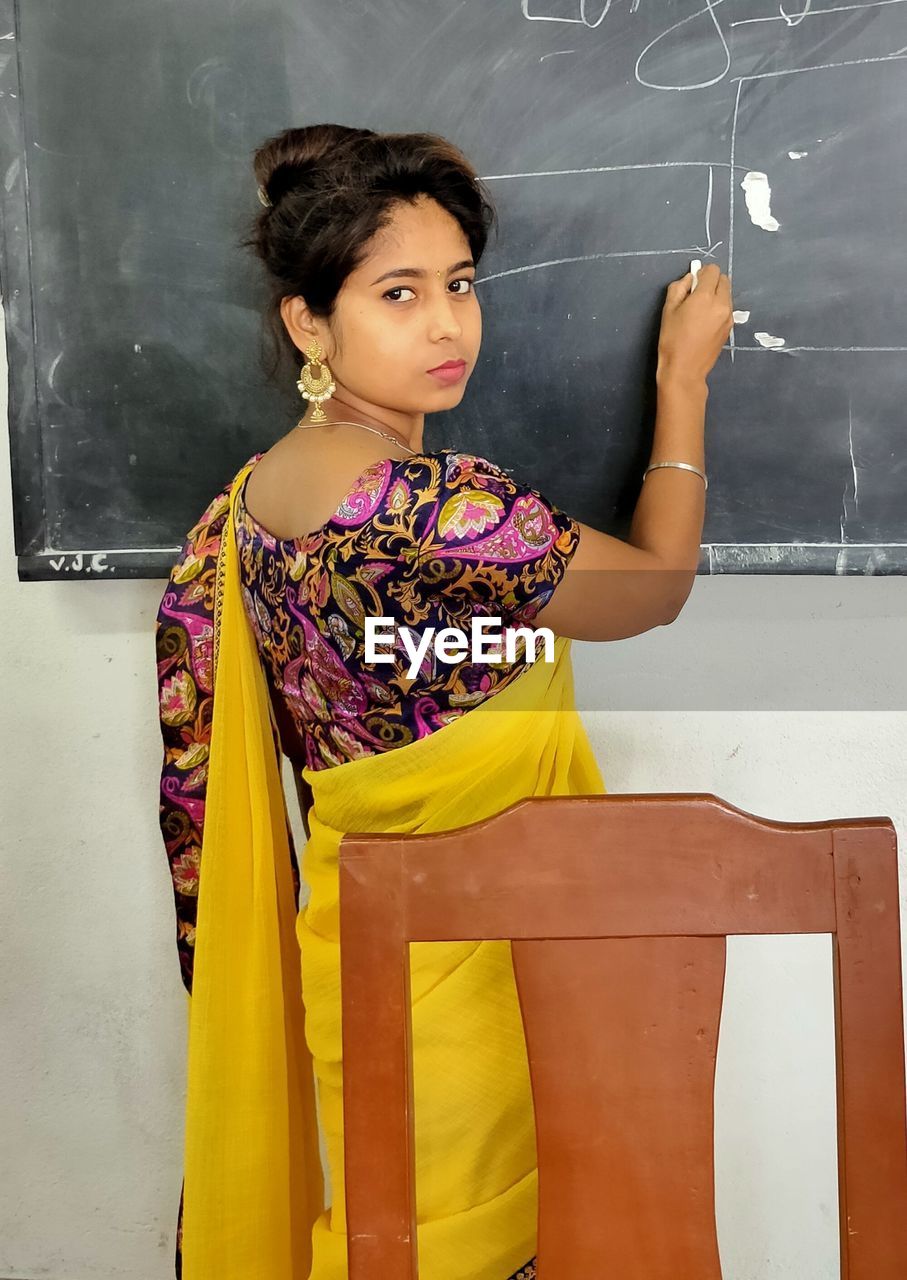 Portrait of young woman drawing on blackboard