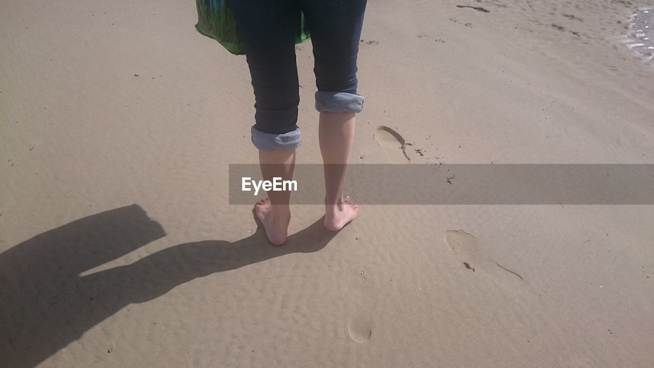 LOW SECTION OF WOMAN STANDING ON SANDY BEACH