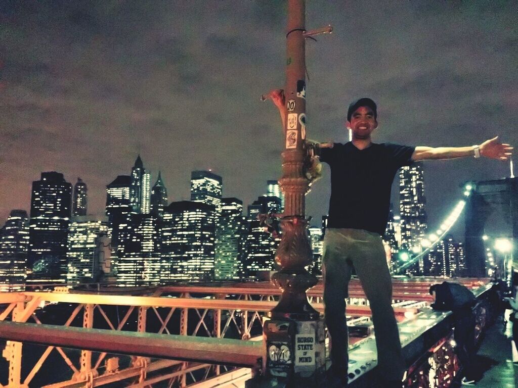 Smiling man standing on bridge against illuminated city