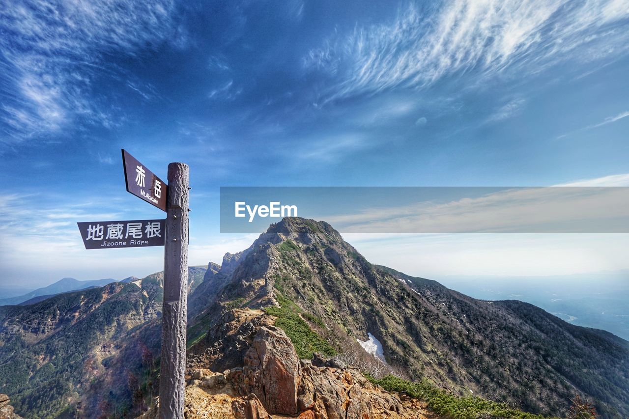 Road sign by mountains against sky