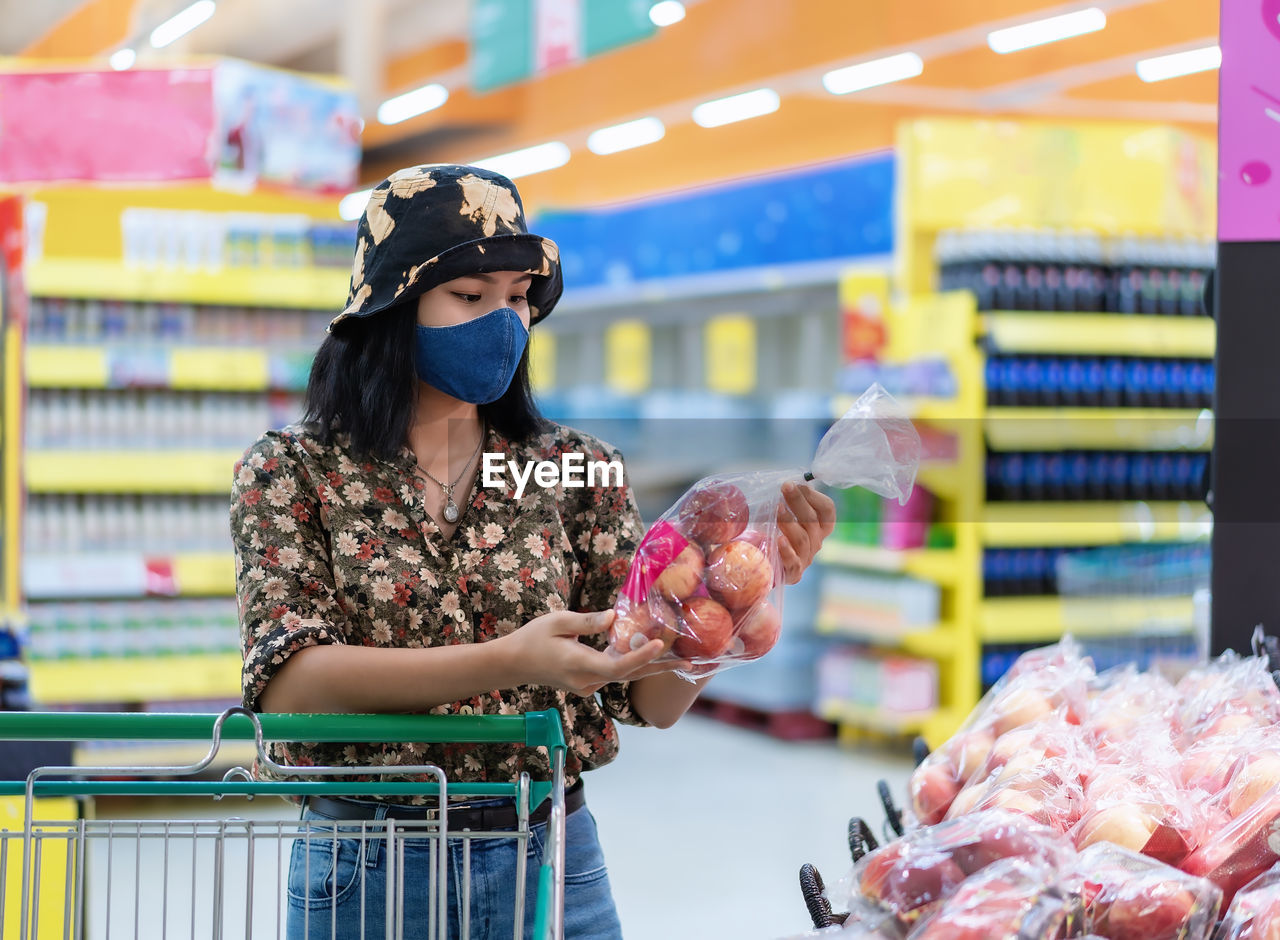 Asian woman wearing face mask shopping and choosing, looking for fruits or grocery things to buy 