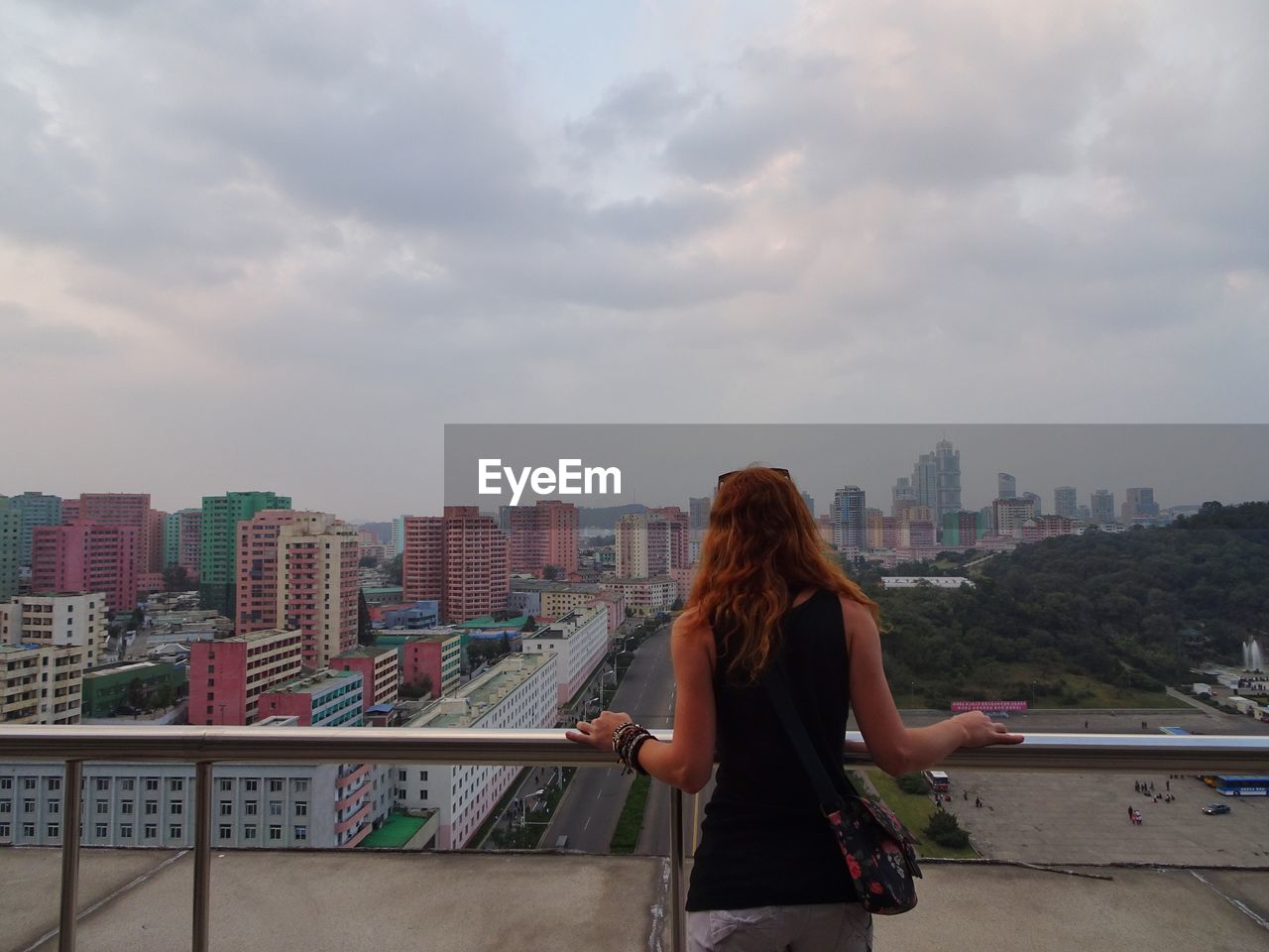 Rear view of woman looking at cityscape against cloudy sky