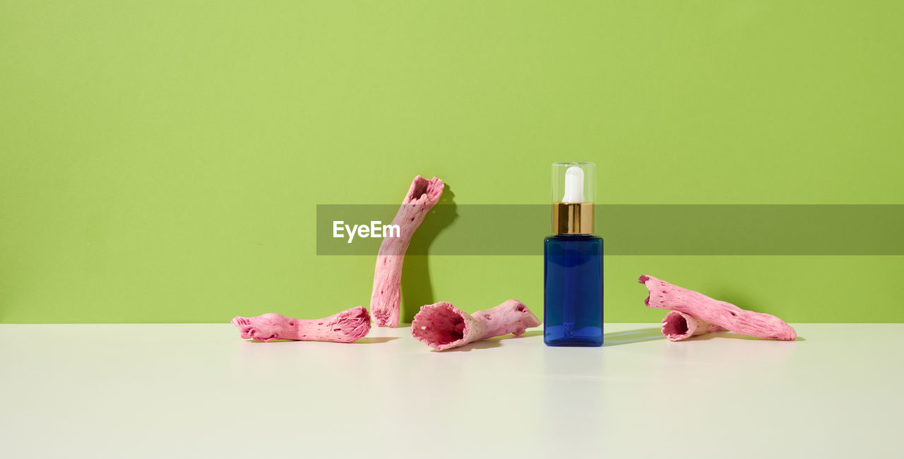 Blue glass bottle with a dropper for cosmetics on a white table, green background. packaging fo