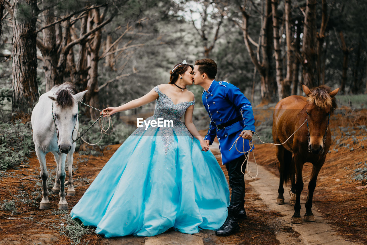 Wedding couple holding horses while kissing on mouth in forest