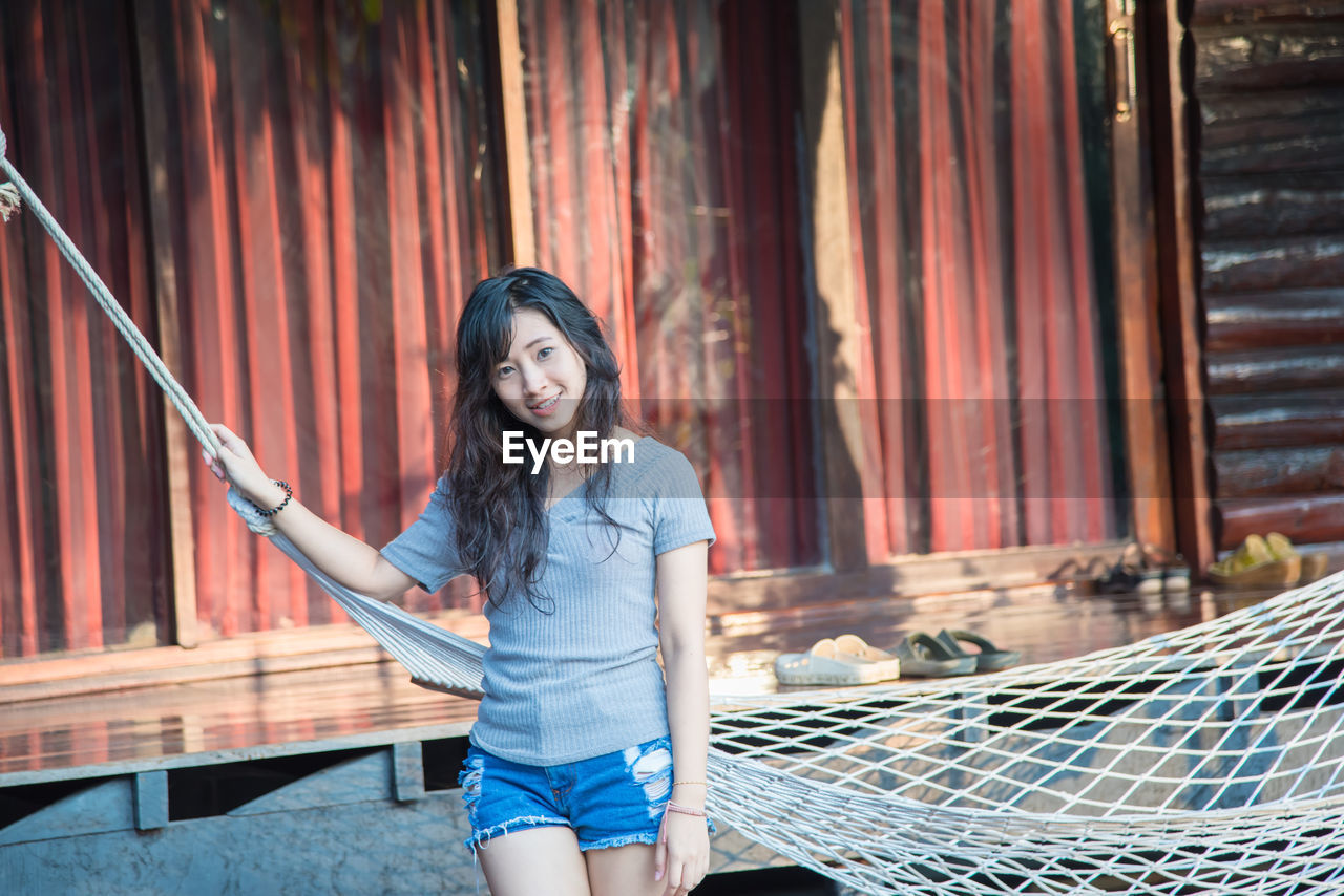 Portrait of young woman standing by hammock