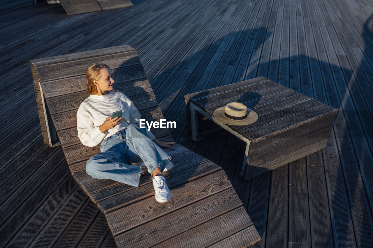 Woman with smart phone sitting on wooden bench