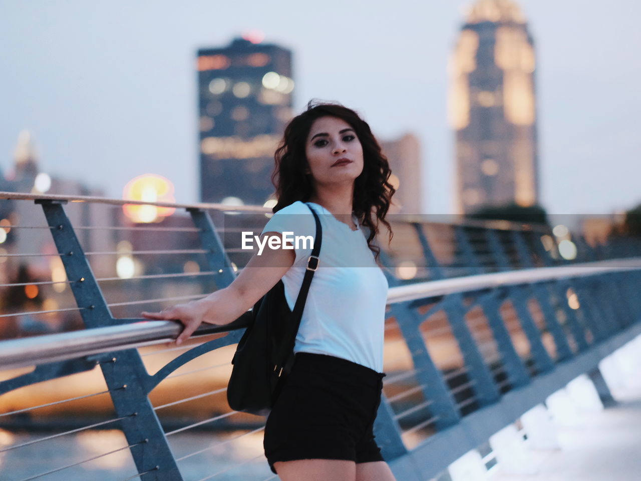 Portrait of woman standing on bridge in city at dusk