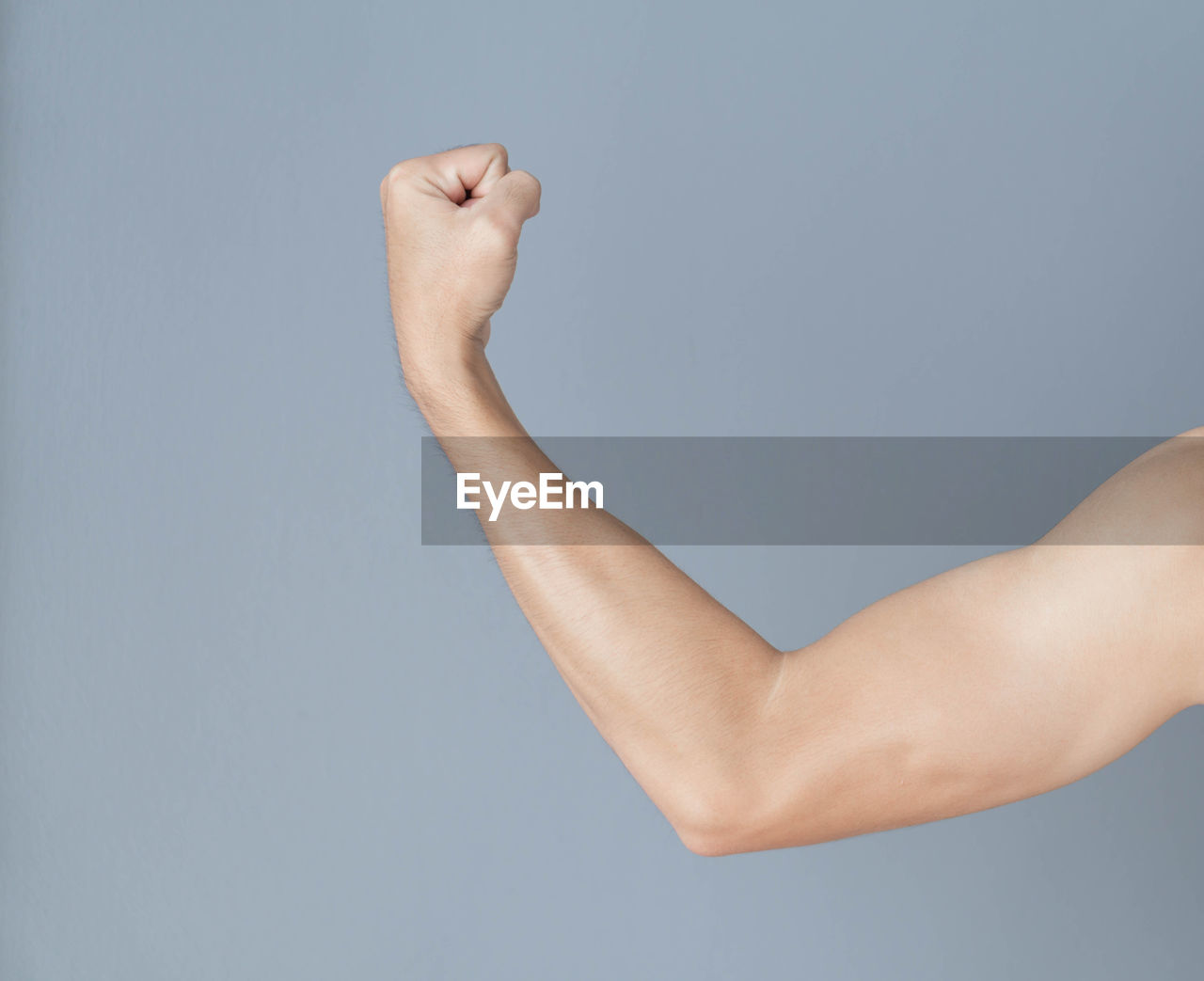 Cropped hand of man flexing muscles over gray background