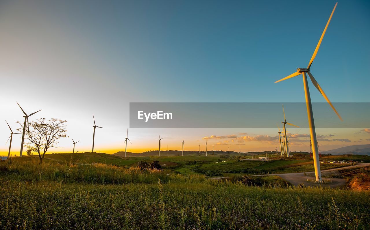 WINDMILLS ON FIELD AGAINST SKY DURING SUNSET