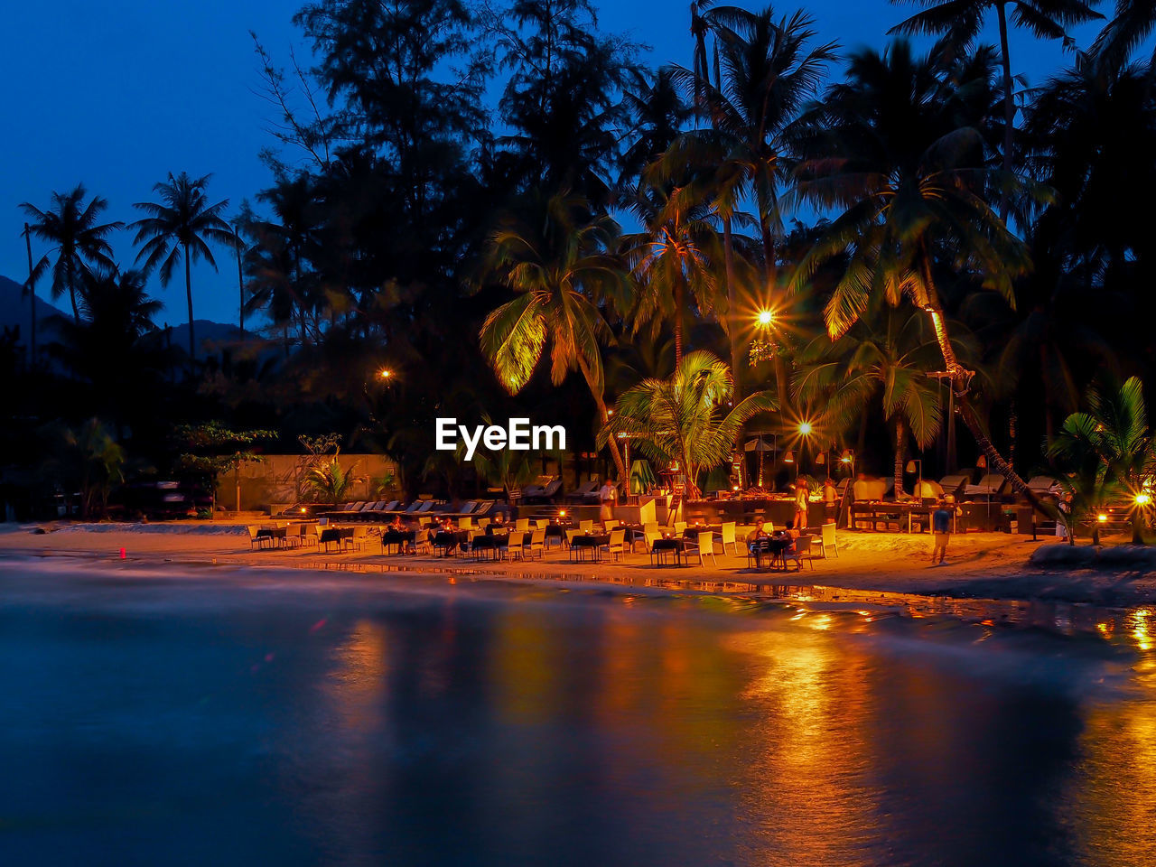 Tables and chairs arranged on illuminated shore at beach