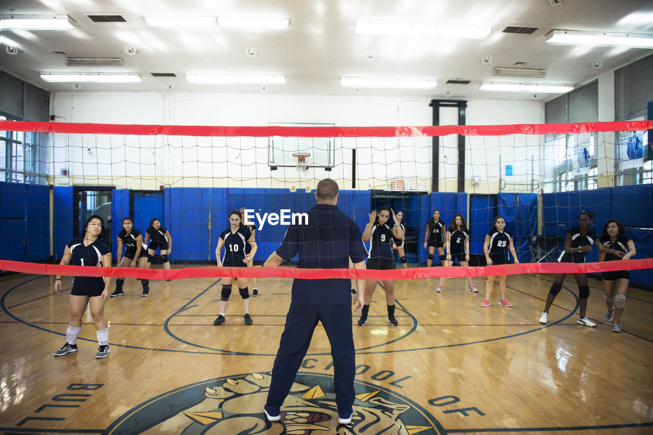 Male coach teaching exercise to female volleyball team