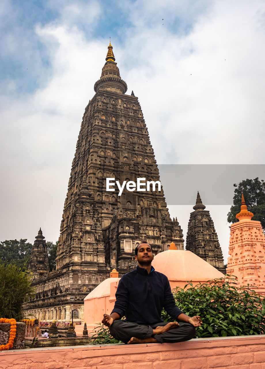 Low angle view of man with eyes closed meditating against temple