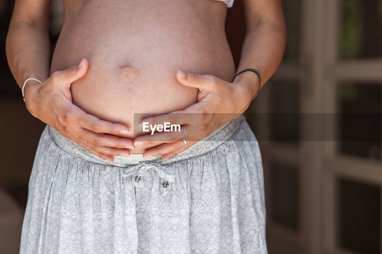 Midsection of pregnant woman standing at home