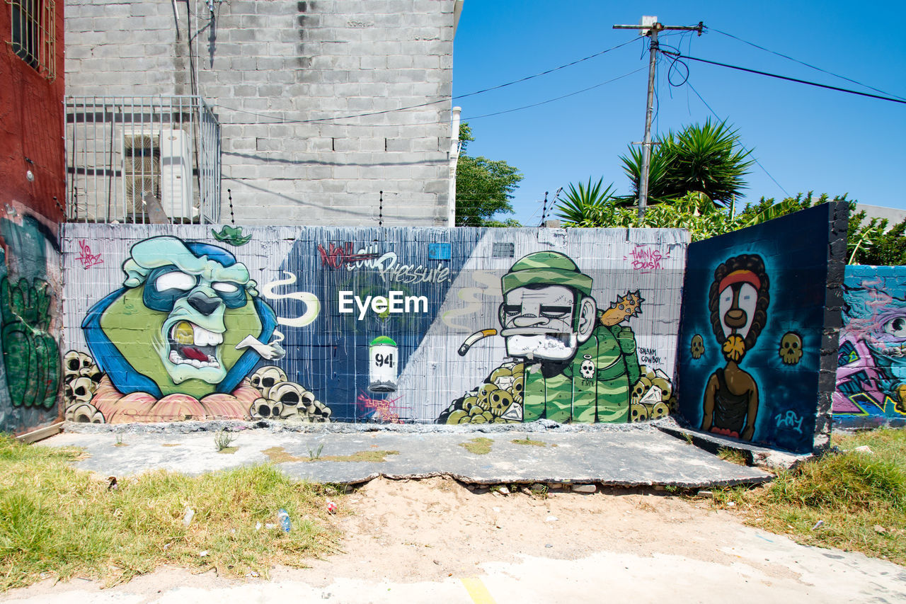 GRAFFITI ON WALL BY PLANTS AGAINST BLUE SKY