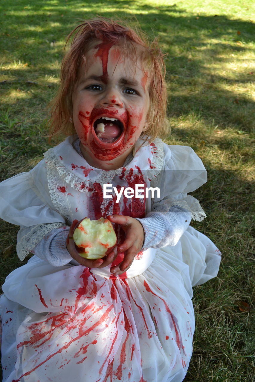 Portrait of girl in halloween costume eating apple while standing on field