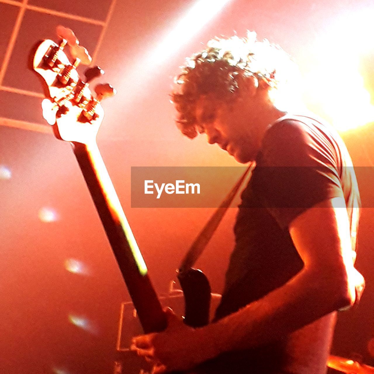 SIDE VIEW OF MAN PLAYING GUITAR IN ILLUMINATED STAGE