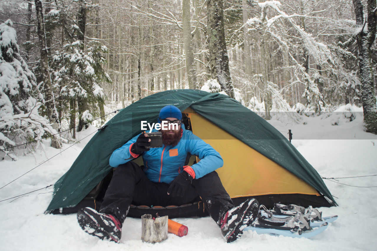 Portrait of young man with coffee sitting in tent on snow covered forest