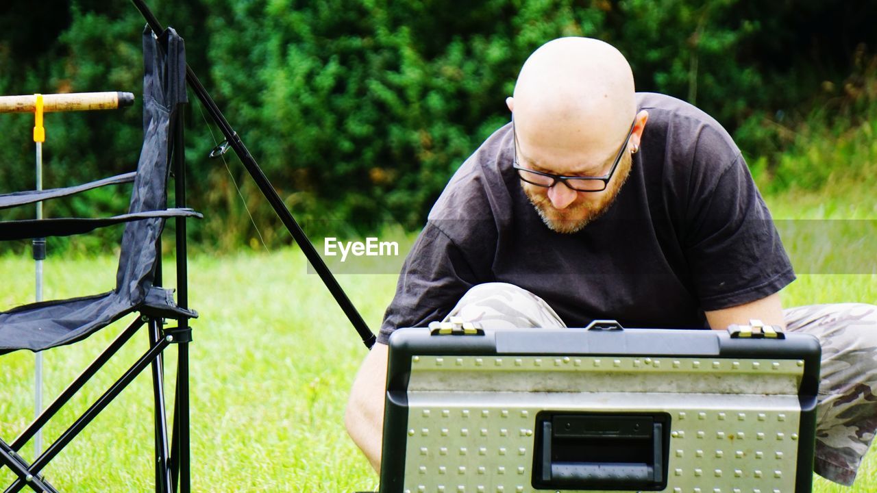 Man looking down by briefcase at grassy field