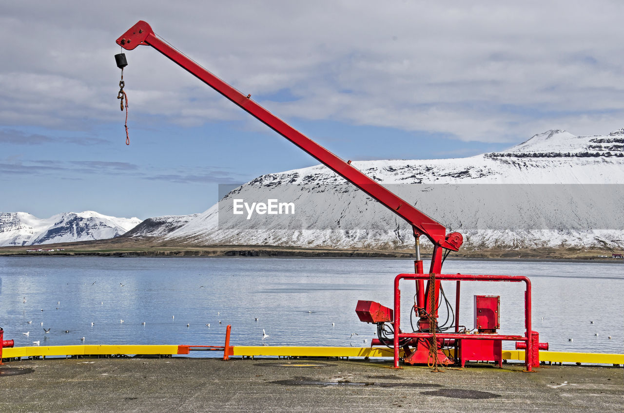 Small harbour crane, painted bright red, with snow-covered mountains in the background