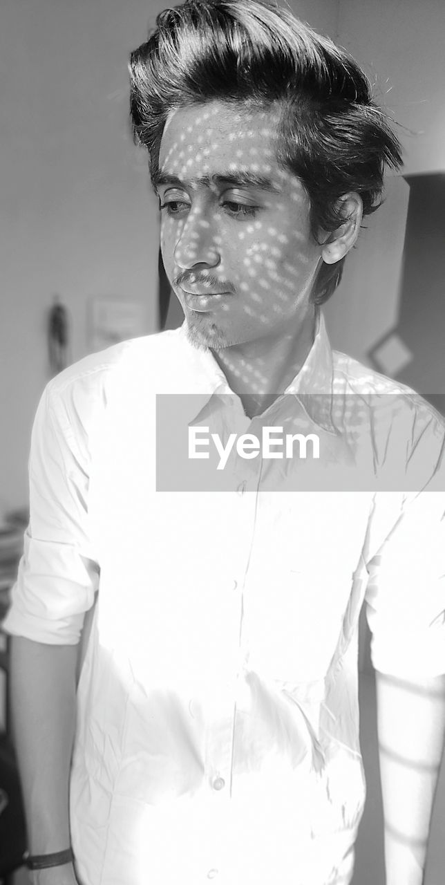 PORTRAIT OF YOUNG MAN LOOKING AWAY WHILE STANDING ON INDOORS