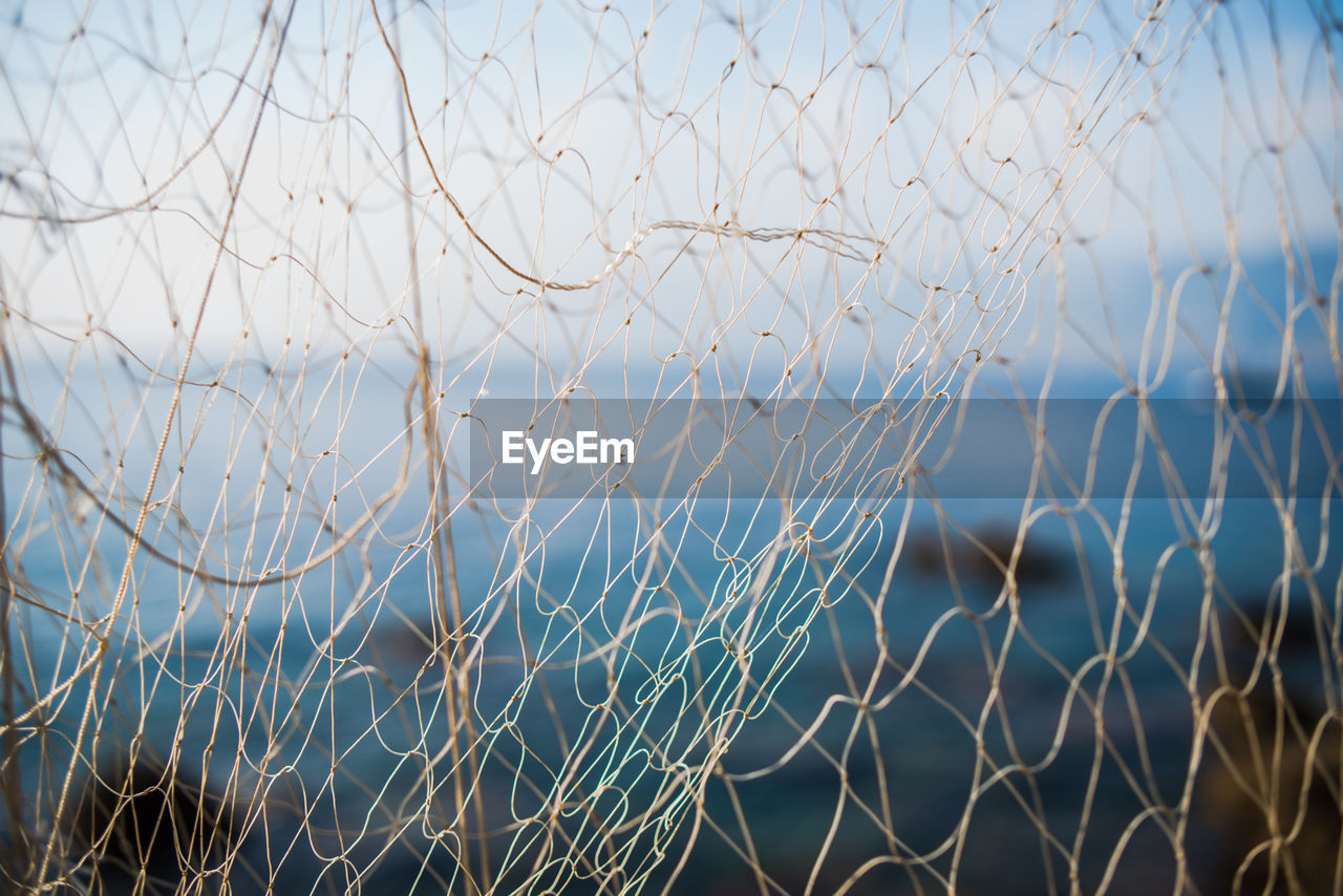 Close-up of fishing net with sea in background