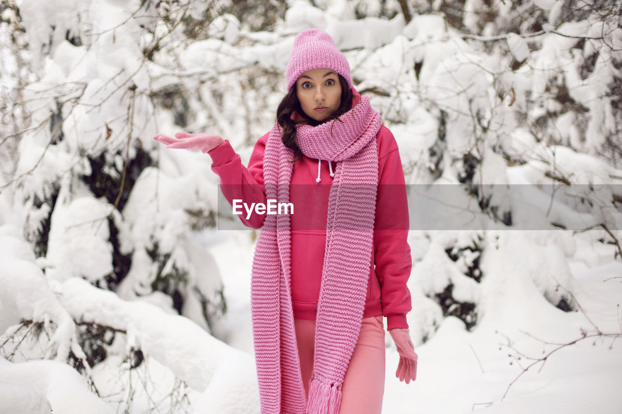 Woman surprise in pink clothes a jacket a knitted scarf and a hat stands in a snowy forest in winter