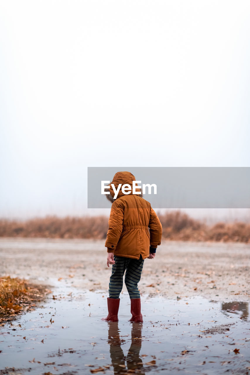 Small boy standing in a mud puddle on a gravel road in the fog