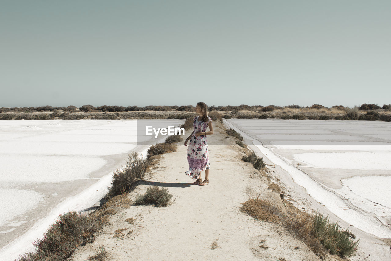 Rear view of woman walking on road against clear sky