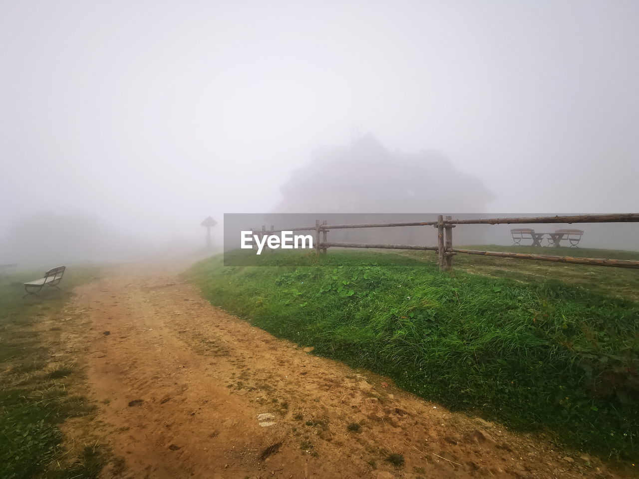 Road amidst field against sky during foggy weather