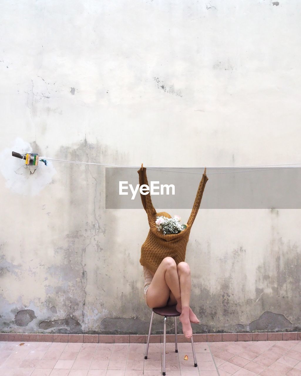 Woman with face covered by flowers sitting on chair against wall