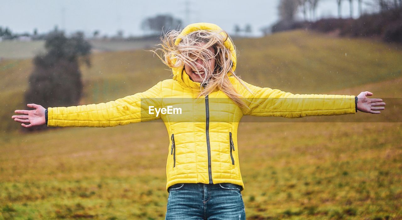 Smiling woman with arms outstretched standing on field