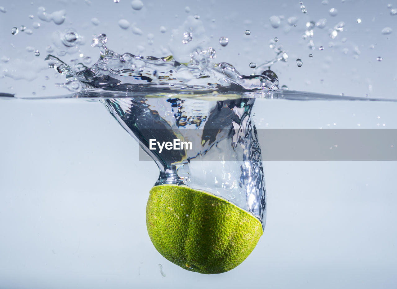 Close-up of limes drops on water against white background