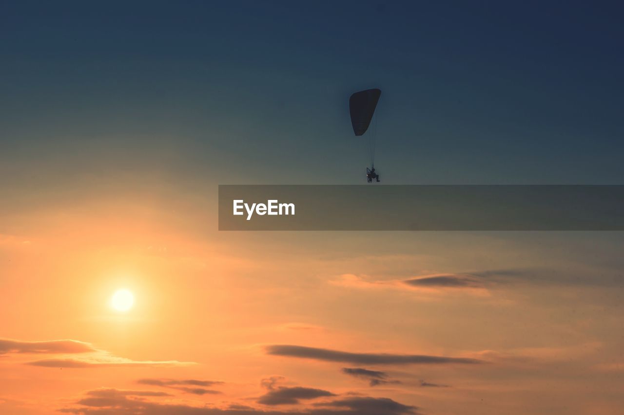 Low angle view of silhouette person paragliding against sky during sunset