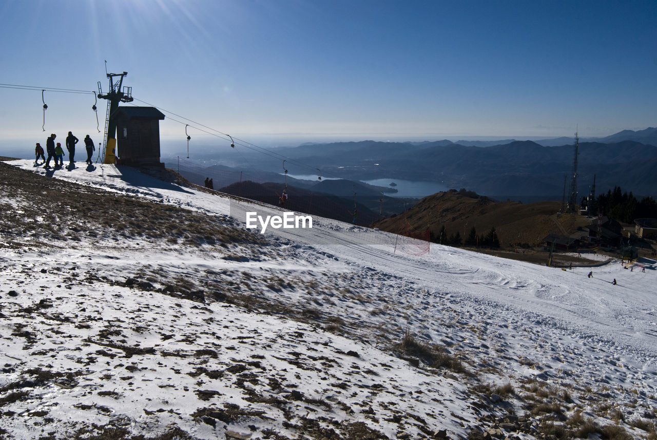 People standing by overhead cable car on snowcapped mountain