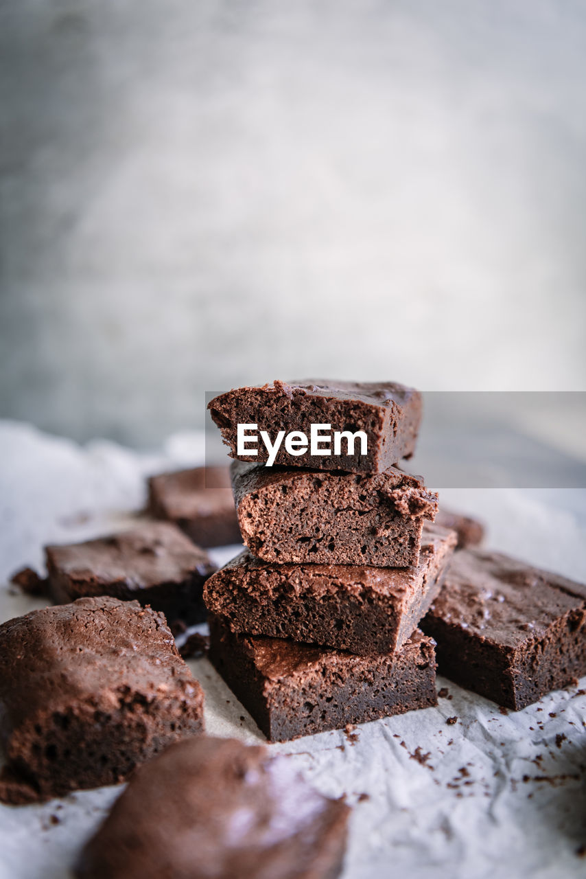 Pile of tasty soft brownie pieces on parchment near shiny wall in house