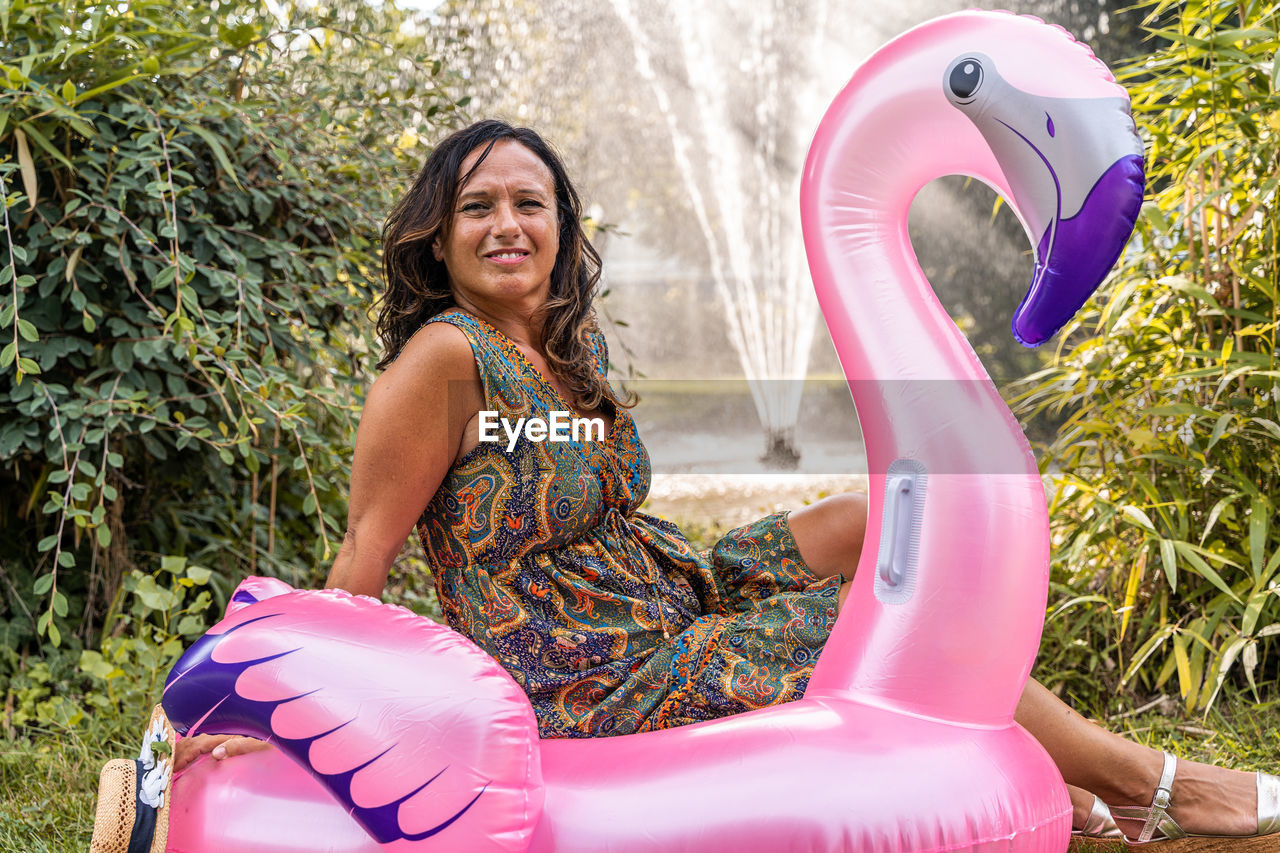 Beautiful smiling middle aged woman having fun sitting on a pink flamingo shaped inflatable toy