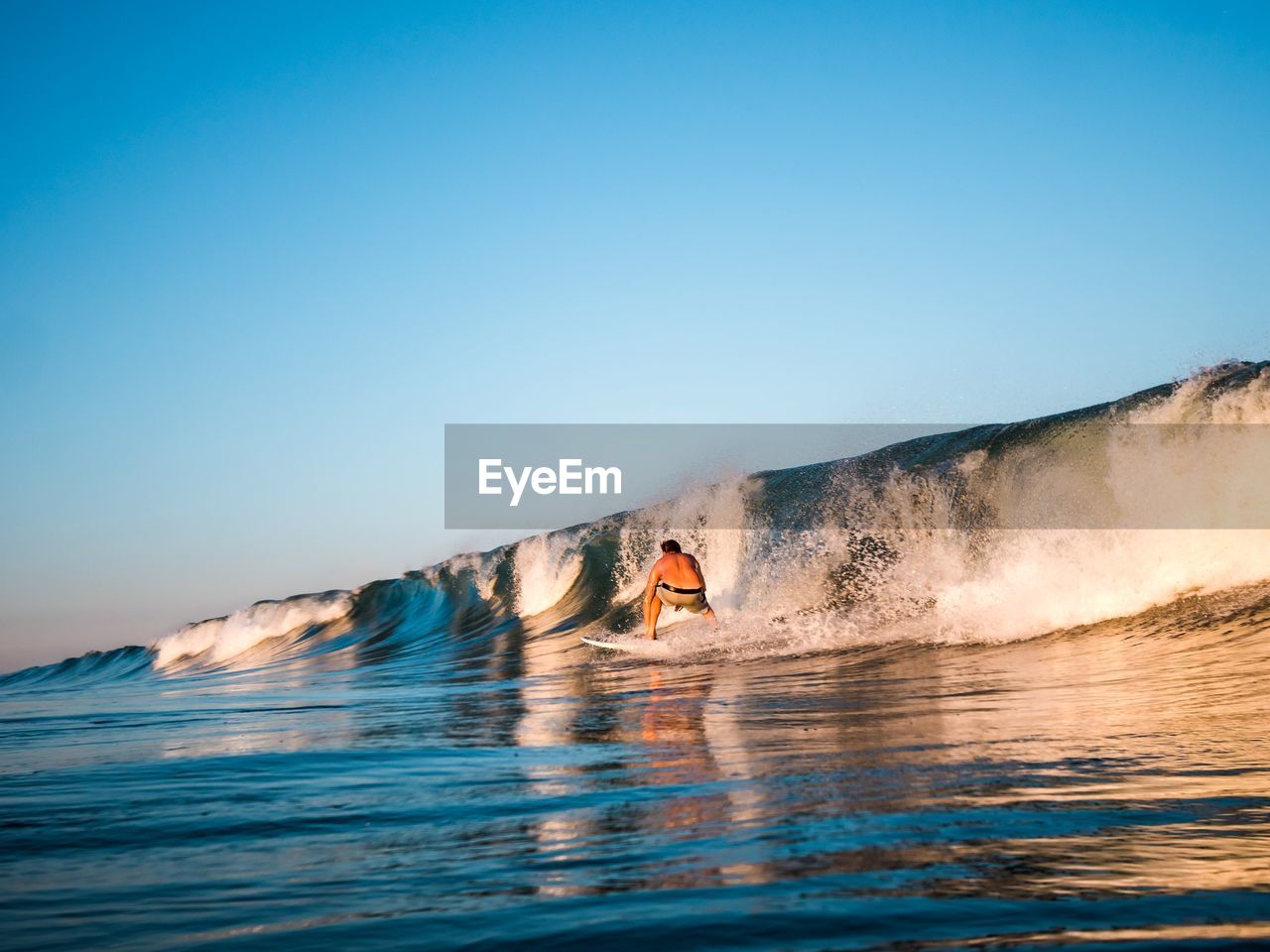 Rear view of shirtless man surfing in sea against clear blue sky