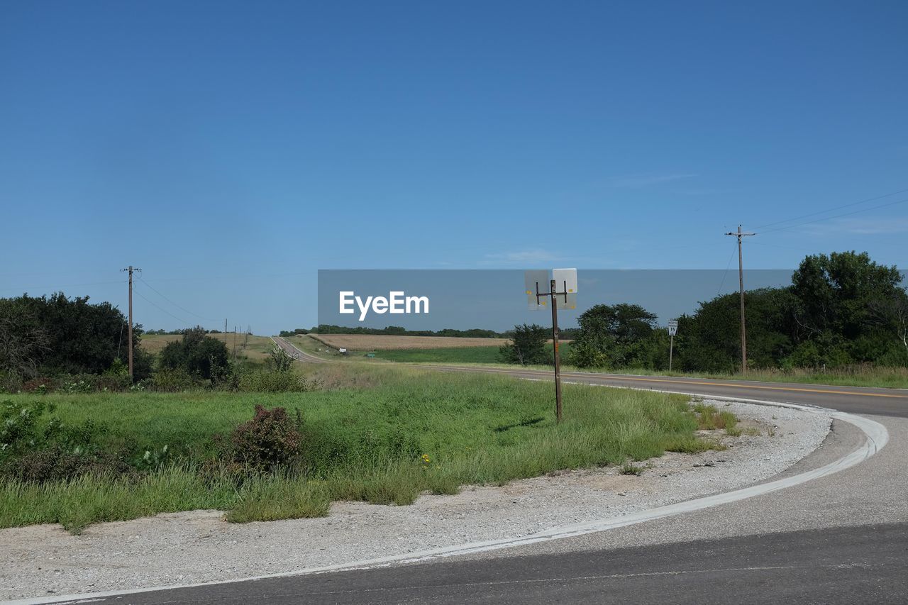 Empty road amidst field against clear sky