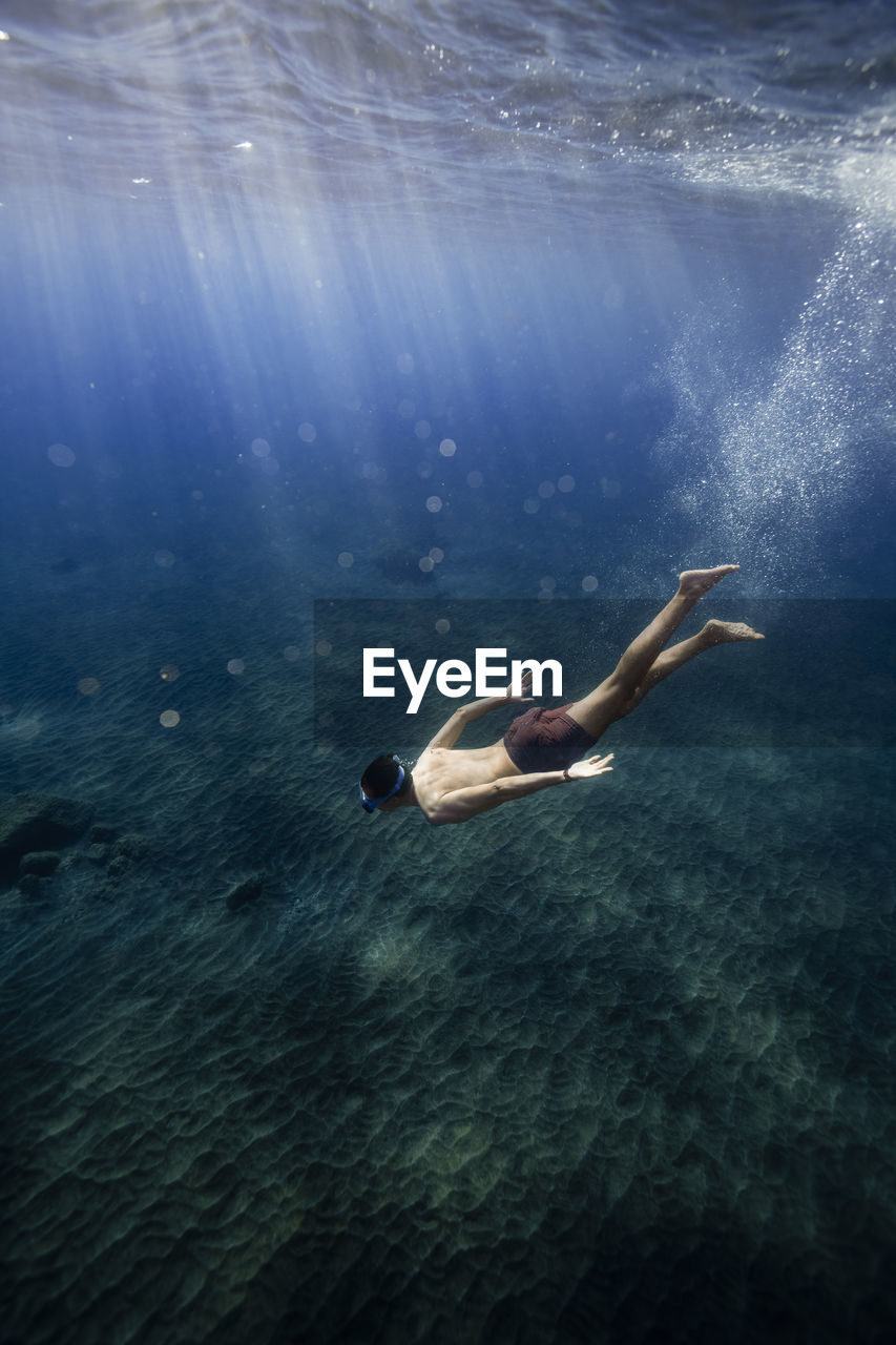 Sunlight on young man swimming over ocean floor in sea