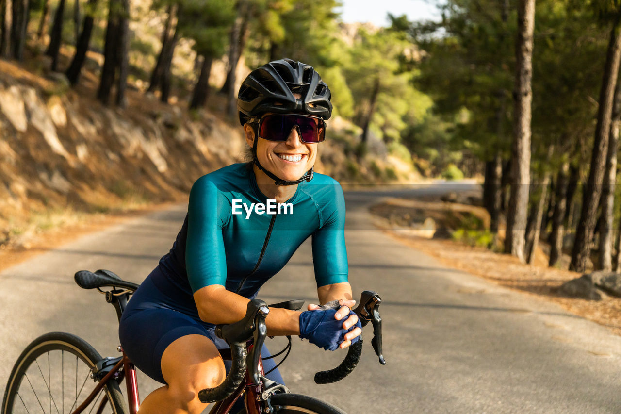 Mature woman training road bike, climbing a mountain road, resting sit on the bike and smile