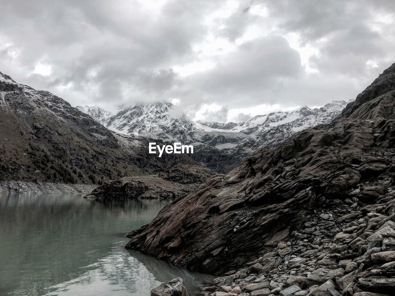 River by rocky mountains against cloudy sky during winter