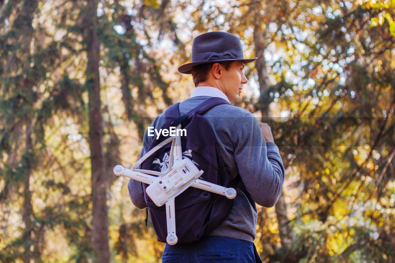 Man with drone standing against trees in forest