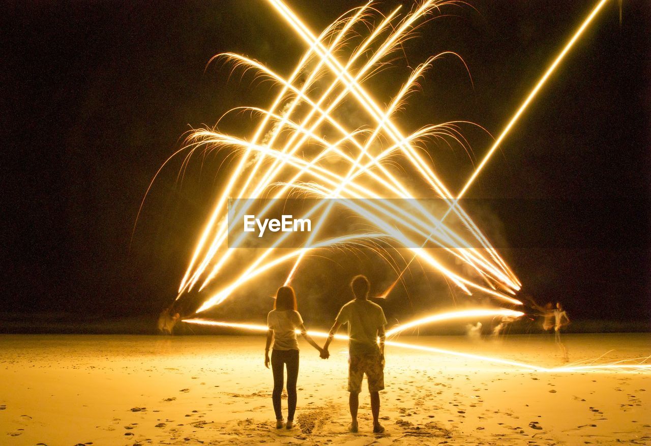 Rear view of man and woman watching light painting on beach at night