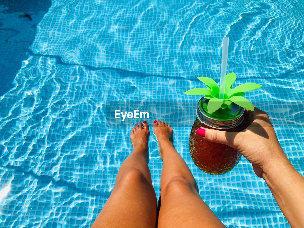 Low section of woman with drink in swimming pool